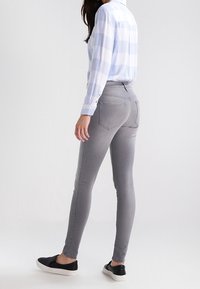 Jeans ajustados de mezclilla gris con una textura suave, combinados con una camisa a cuadros de color azul claro. El calzado son zapatos de slip-on negros.