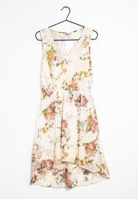 Blommig klänning med en krämig beige bakgrund, prydd med mönster av rosa och gröna rosor, med V-ringning och spetsdetaljer. Hänger på en svart krok.