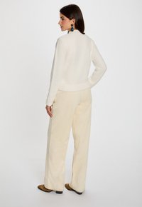 Crème gekleurde trui met een nauwsluitende taille, gecombineerd met hooggeplaagde wijde corduroy broek in lichtbeige. Bruine enkelboots inbegrepen.