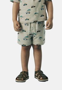 Beige kortærmet skjorte og matchende shorts med farverige mønstre af biler og dyr. Brune sandaler med et snore-design.
