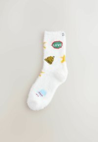 Fuzzy hvid sok med farverige mønstre: et grønt "KÆRLIGHED", en gul stjerne, en blå form og et leopardprint-detalje. Blød tekstur.