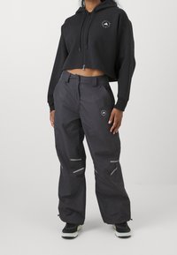 Černá zkrácená mikina s předním zipem, se zaobleným logem. V kombinaci s tmavě šedými kalhotami, reflexními detaily a elastickým pasem.