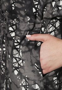 Černo-bílá látka s geometrickými tvary; obsahuje nastavitelný pás a boční kapsu. Hladká, saténová textura.