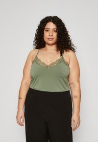 Olivgrüner Camisole mit Spitzenbesatz und verstellbaren Spaghetti-Trägern, kombiniert mit schwarzen Hose mit elastischem Bund für eine lässige Passform.