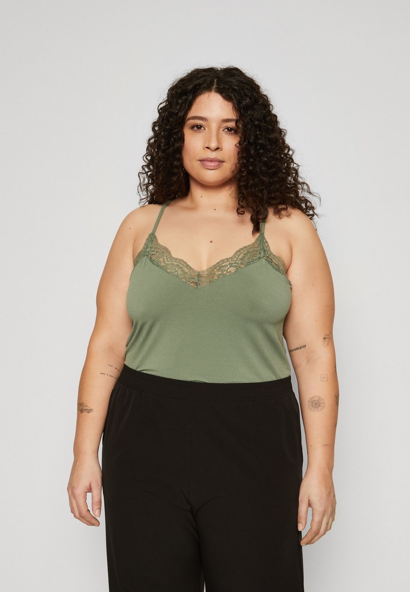Olivgrüner Camisole mit Spitzenbesatz und verstellbaren Spaghetti-Trägern, kombiniert mit schwarzen Hose mit elastischem Bund für eine lässige Passform.