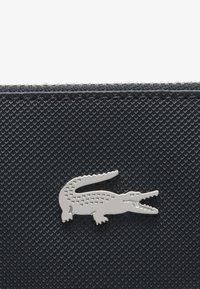 Portefeuille texturé bleu marine avec un logo en crocodile argenté. Le motif en diamant distinctif ajoute de la profondeur, accompagné d'un bord de fermeture éclair lisse pour plus de fonctionnalité.
