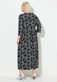Vestido maxi negro con un patrón floral blanco, con mangas tres cuartos, cintura ajustada y falda fluida. Combinado con tacones plateados.