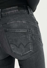Jeans de mezclilla negra con un diseño ajustado, bolsillos traseros prominentes y un patrón de costura distintivo en el bolsillo trasero.