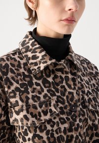 Veste en imprimé léopard beige et noir, avec un col, une fermeture à boutons et deux poches poitrine en tissu texturé.