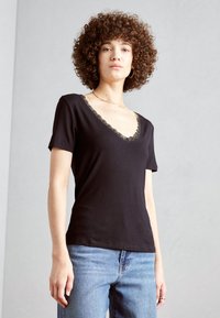 Svart T-skjorte med V-hals og blondekant, korte ermer og en tettsittende design. Kombinert med blå denim jeans.
