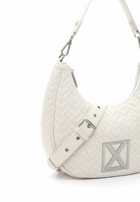 Witte gequiltte handtas met visgraatstructuur, zilveren hardware, een ritssluiting en een verstelbare schouderriem. Heeft een logo-plaat aan de voorkant.