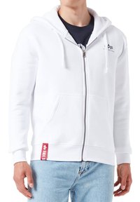 Felpa bianca con zip realizzata in cotone, con tasca frontale, cappuccio regolabile e un'etichetta rossa sull'orlo. Design casual, texture liscia.