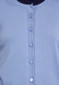 Světle modrý pletený cardigan s kulatým výstřihem, středním zapínáním na modré knoflíky a hladkou texturou.