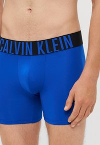 Boxer da uomo blu con un elastico nero in vita su cui è riportato "CALVIN KLEIN" in lettere blu; tessuto morbido e vestibilità aderente.