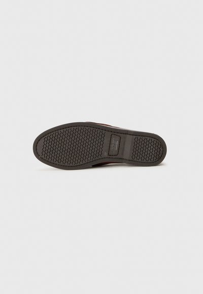 Suola di scarpa in gomma marrone con un pattern di presa testurizzato. Presenta una toppa con logo rettangolare e bordi curvi. Design minimalista, colori neutri.
