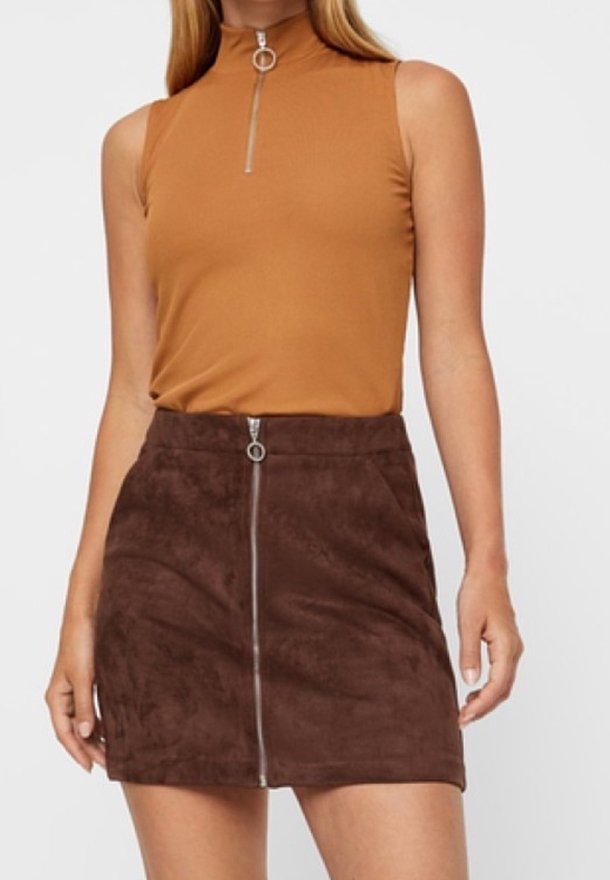 Mini-jupe en faux suede marron avec une fermeture éclair centrale et un anneau, associée à un haut sans manches beige avec un col montant et une fermeture éclair argentée.