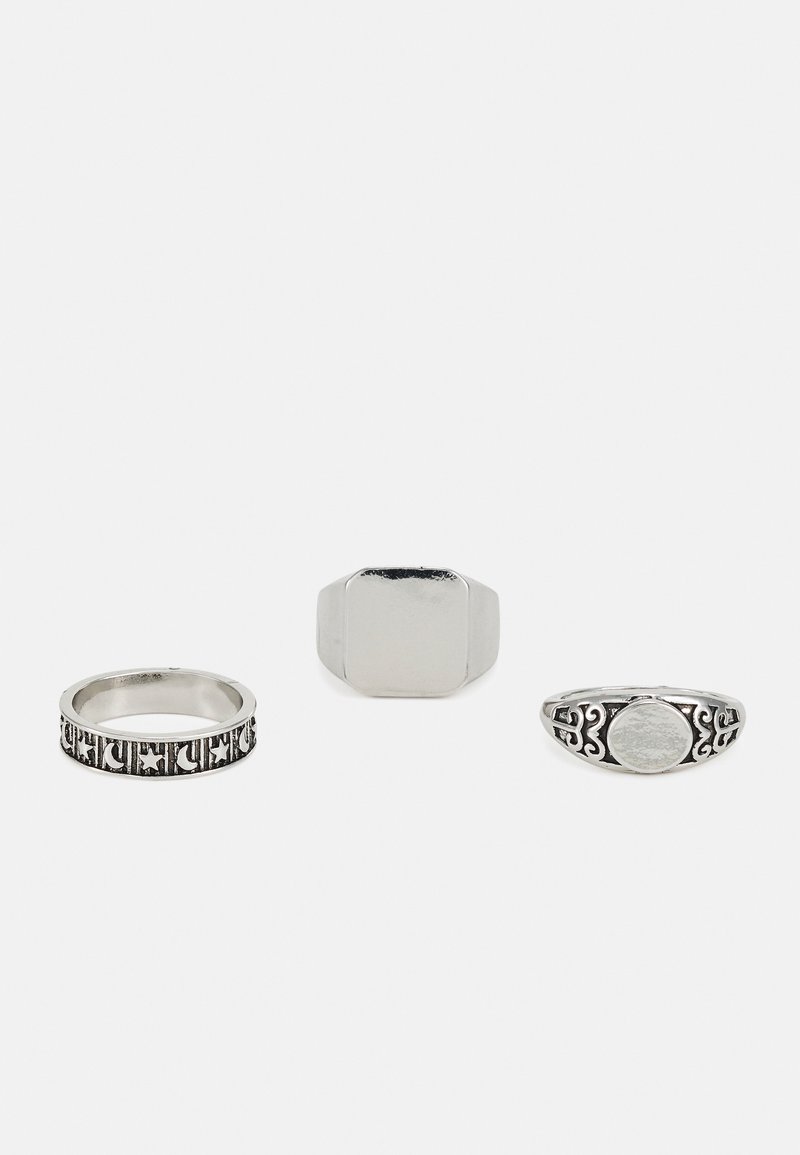 Três anéis de prata: um com uma banda decorada, um design retangular liso e um com um centro oval texturizado e detalhamento ornamentado.