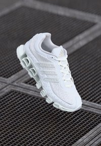 Hvit sportsko med pustende mesh-overdel, tykk lys grønn såle og tre hevede striper på siden; avrundet tådesign.