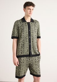 Short-sleeve patterned shirt and matching shorts in green and black, featuring a reptile-like design, black trim, and button front closure.
