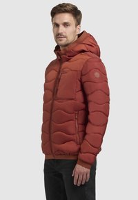 Röd isolerad jacka med vågmönster, dragkedja framtill, huva, ficka framtill och ribbade ärmslut. Slät textur och figurnära design.