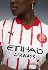 Wit voetbalshirt met rode horizontale strepen, rode kraag en zwart Puma-logo. Bevat "ETIHAD AIRWAYS" in vet zwart en het clubembleem van Girona.