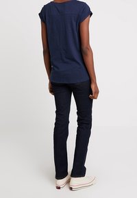 Top de manga corta en color navy con puños enrollados, combinado con jeans oscuros de mezclilla y zapatillas blancas de corte bajo. El conjunto presenta un ajuste relajado y líneas limpias.