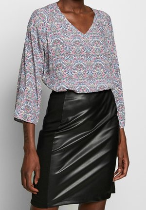 Mujer con blusa floral de manga larga y cuello en V metida dentro de una falda lápiz negra con aspecto de cuero.
