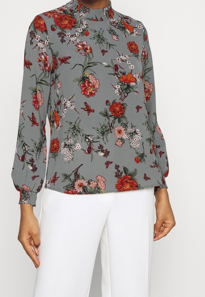Graue Bluse mit floralen Mustern, langen Ärmeln, gerafftem Kragen und bunten Blumen- und Schmetterlingsmotiven. Schicke Textur mit elastischen Bündchen.