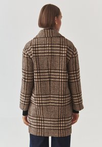 Wool blend coat with a brown, black, and cream check pattern. Features a wide collar, long sleeves, and a knee-length cut. Textured finish.