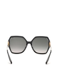 Lunettes de soleil hexagonales noires oversize avec des accents dorés sur les branches et des verres dégradés gris, vues de face sur fond blanc.