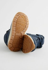 Chaussures bleu marine avec un dessus en synthétique texturé, présentant une semelle en caoutchouc avec un motif en zigzag et un col de cheville rembourré pour le soutien.