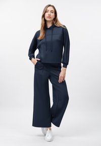 Haut à capuche court bleu marine avec une poche à l'avant et des cordons de serrage ajustables, associé à un pantalon large bleu marine, le tout en tissu lisse.