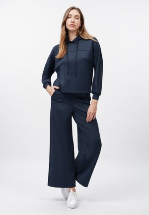 Navy blue cropped hoodie with a front pocket and adjustable drawstrings, paired with wide-leg navy pants, all in a smooth fabric.