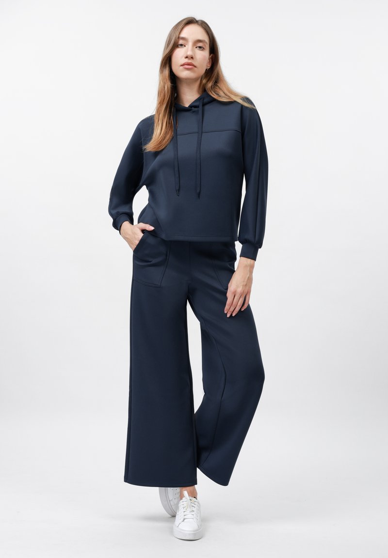 Haut à capuche court bleu marine avec une poche à l'avant et des cordons de serrage ajustables, associé à un pantalon large bleu marine, le tout en tissu lisse.