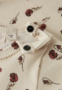 Body in cotone per neonati con una texture a coste color crema, caratterizzato da motivi floreali rossi e bottoni a pressione neri sul collo. Taglia 4-6 mesi.