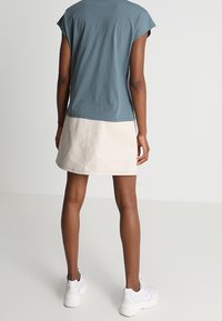 Jasnoniebieska koszulka z krótkim rękawem w połączeniu z beżową mini spódnicą o gładkiej fakturze, noszona z białymi trampkami.