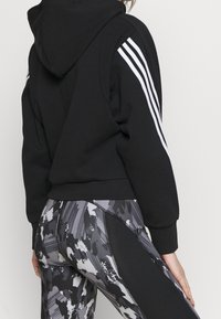 Sudadera negra con rayas blancas en las mangas. Combinada con leggins grises estampados que presentan diseños de pinceladas y acentos negros en contraste.