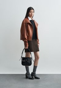 Brown leather biker jacket, black sweater, brown skirt, black handbag with studs, gray socks, and shiny black heels, set against a neutral background.