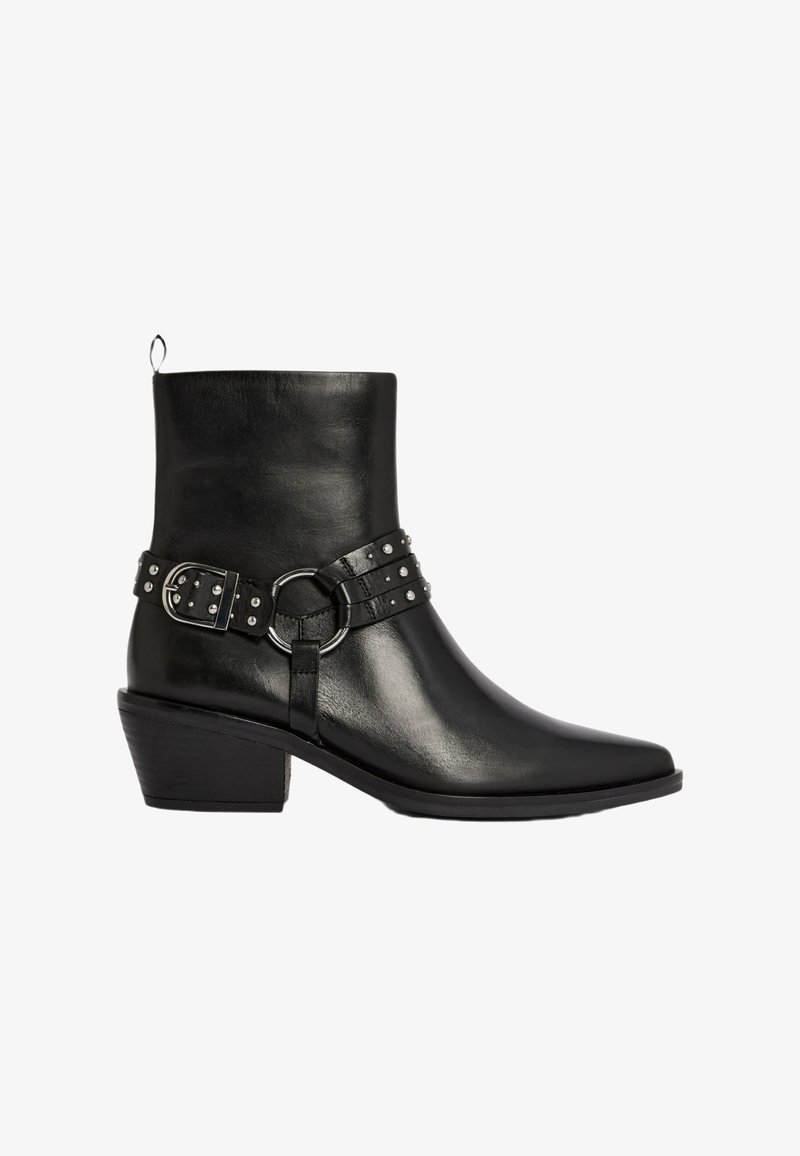 Schwarze Leder-Stiefelette mit spitz zulaufender Zehenpartie, gestapeltem Absatz, silberner Schnallenriemen und Nietenakzenten im Gürtel-Detail. Glatte Oberfläche.