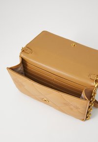 Quiltet lysebrun læderhåndtaske med guldhardware; har en klaplukning, flere kortlommer indeni og en kæde skulderrem.