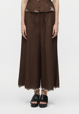 Καφέ φαρδιά παντελόνια cropped με σκαλοειδές και διακοσμητικό τελείωμα, φορεμένα με μαύρα πέδιλα πλατφόρμας με ανοιχτά δάχτυλα σε λευκό φόντο.