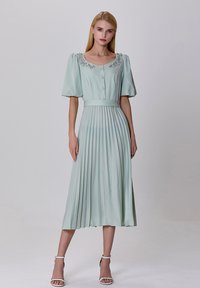 Robe midi plissée vert clair avec des manches courtes bouffantes, un décolleté carré et des détails décoratifs en perles au col.