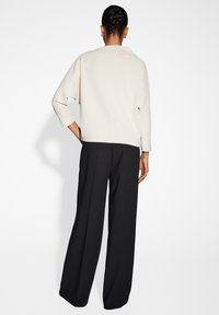 Pullover beige chiaro con vestibilità rilassata e maniche a tre quarti, abbinato a pantaloni larghi neri, visto da dietro.