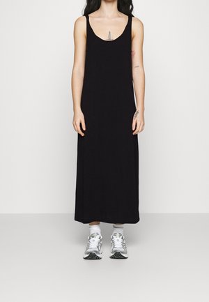 Zwarte mouwloze maxi-jurk met een ronde hals en een losse pasvorm. Gecombineerd met zilveren sportieve sneakers en witte crew-sokken.