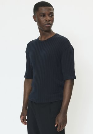 Marineblå ribstrikket skjorte med korte ærmer, rund hals, blød tekstur og tætsiddende design, kombineret med mørke bukser.