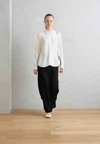 Cămașă albă cu mânecă lungă și nasturi, asortată cu o fustă lungă neagră. Outfitul are un fit lejer și un material neted, creând o siluetă elegantă.
