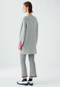 Grauer übergroßer Pullover mit rosa Bündchen, kombiniert mit grauen cropped Jeans und silbernen Schuhen, mit einer glatten Textur und lockerer Passform.