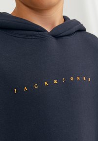 Felpa navy con cappuccio, con il testo arancione "JACK & JONES" sul petto. Tessuto di cotone liscio e dettaglio a costine sul collo.