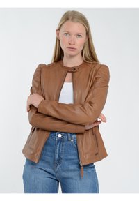 Brun läderjacka med rund hals, kviltade axeldetaljer och dragkedja framtill. Kombinerad med högmidjade blå jeans.