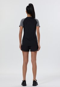 T-shirt de sport noire avec des manches raglan grises, associée à un short noir. Texture lisse, design décontracté, adapté pour le sport ou l'exercice.
